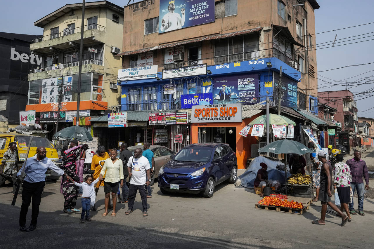 People walk past sports betting shops on a street in Lagos, Nigeria, Monday, Dec. 5, 2022. Although...