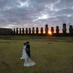 
              Newlyweds Daniela Figueroa and Ricardo Torres stand in an embrace as they take in a sunrise peeking through moai statues while their tour guide makes a photo of them, on Ahu Tongariki, Rapa Nui, or Easter Island, Chile, on Nov. 22, 2022. (AP Photo/Esteban Felix)
            