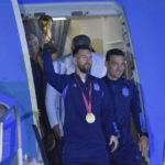 
              Argentina's Lionel Messi hoists the FIFA World Cup trophy as he deplanes, with coach Lionel Scaloni, in Buenos Aires, Argentina, Tuesday, Dec. 20, 2022. (AP Photo/Gustavo Garello)
            