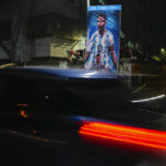 
              A car passes a poster of Argentina's Leonel Messi, erected by the Indian fans of Argentina during the World Cup semi final soccer match between Argentina and Croatia in Qatar, Wednesday, Dec. 14, 2022. Argentina defeated Croatia 3-0. (AP Photo/Bikas Das)
            