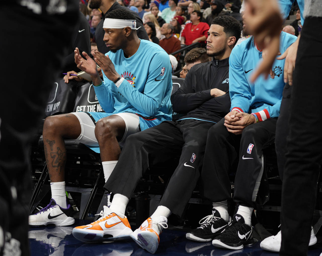 Phoenix Suns guard Devin Booker, wearing black, sits on the bench next to forward Torrey Craig in t...