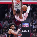 
              Chicago Bulls forward Derrick Jones Jr., top, hangs from the rim after dunking as Golden State Warriors forward Anthony Lamb runs on the court during the first half of an NBA basketball game in Chicago, Sunday, Jan. 15, 2023. (AP Photo/Nam Y. Huh)
            