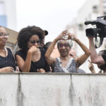 
              Maria Lucia Nascimento, the sister of the late Brazilian soccer great Pele, signals a heart to people gathered outside her mother's home, during Pele's funeral procession from Vila Belmiro stadium to the cemetery in Santos, Brazil, Tuesday, Jan. 3, 2023. (AP Photo/Matias Delacroix)
            