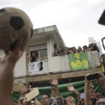 
              People watch the funeral procession of Brazilian soccer great Pele pass by the home of Pele's mother, where members of his family stand on the balcony, as his remains are taken from Vila Belmiro stadium to the cemetery in Santos, Brazil, Tuesday, Jan. 3, 2023. (AP Photo/Matias Delacroix)
            