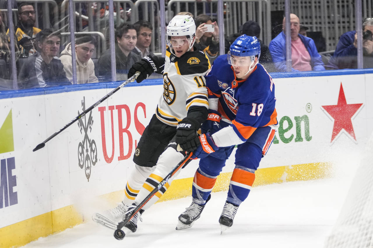 Boston Bruins' Trent Frederic (11) fights for control of the puck with New York Islanders' Anthony ...