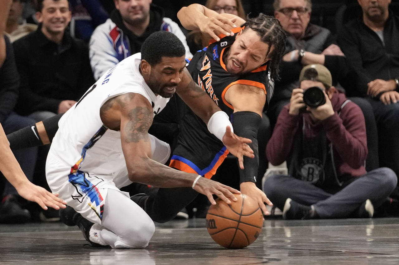 Brooklyn Nets guard Kyrie Irving, left, and New York Knicks guard Jalen Brunson fight for a loose b...
