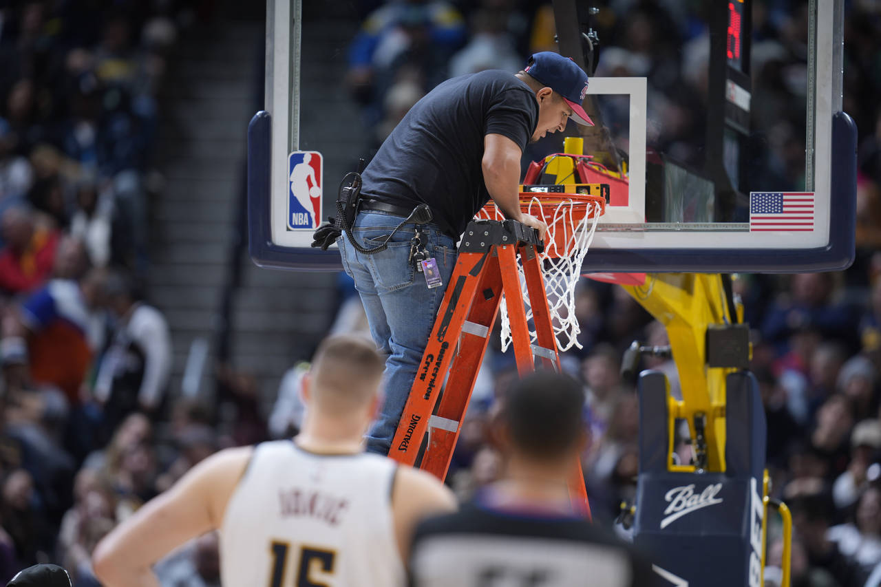 A worker uses a level to check the rim after it was bent by a dunk by Boston Celtics center Robert ...