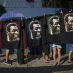 
              Shirts featuring Pele hang for sale where people wait in line to enter Vila Belmiro stadium where the late Brazilian soccer great lies in state in Santos, Brazil, Monday, Jan. 2, 2023. (AP Photo/Matias Delacroix)
            