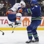 
              New York Islanders' Ross Johnston (32) leaps out of the way to avoid being hit by the puck as Vancouver Canucks' Luke Schenn (2) defends during the second period of an NHL hockey game Tuesday, Jan. 3, 2023, in Vancouver, British Columbia. (Darryl Dyck/The Canadian Press via AP)
            