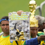 
              Fans hold up photos of the late Brazilian soccer great Pele as they line up at Vila Belmiro stadium where his body lies in state, to pay their last respects in Santos, Brazil, Monday, Jan. 2, 2023. (AP Photo/Andre Penner)
            