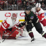 
              Arizona Coyotes center Barrett Hayton (29) controls the puck in front of Detroit Red Wings goaltender Magnus Hellberg (45) as Red Wings defenseman Ben Chiarot (8) looks on during the first period of an NHL hockey game in Tempe, Ariz., Tuesday, Jan. 17, 2023. (AP Photo/Ross D. Franklin)
            