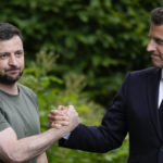 
              FILE - Ukraine President Volodymyr Zelenskyy, left, and France's President Emmanuel Macron shake hands at the end of a press conference at the Mariyinsky Palace in Kyiv, Ukraine, Thursday, June 16, 2022. The question of if and how Russia competes at the Olympics hangs over the 2024 Paris Summer Games. Just as it has now for five straight Olympics during Thomas Bach’s leadership of the IOC. The Bach-led International Olympic Committee's support this week for some Russians to compete in Paris as neutrals was publicly challenged Friday, Jan. 27, 2023 by Ukrainian President Volodymyr Zelenskyy.  (AP Photo/Natacha Pisarenko, File)
            