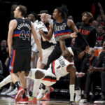 
              Portland Trail Blazers forward Jerami Grant, bottom, watches as he hits a shot while falling down in front of the Blazers bench, as Detroit Pistons forward Bojan Bogdanovic, left, and guard Jaden Ivey, top, look on during the second half of an NBA basketball game in Portland, Ore., Monday, Jan. 2, 2023. (AP Photo/Steve Dykes)
            