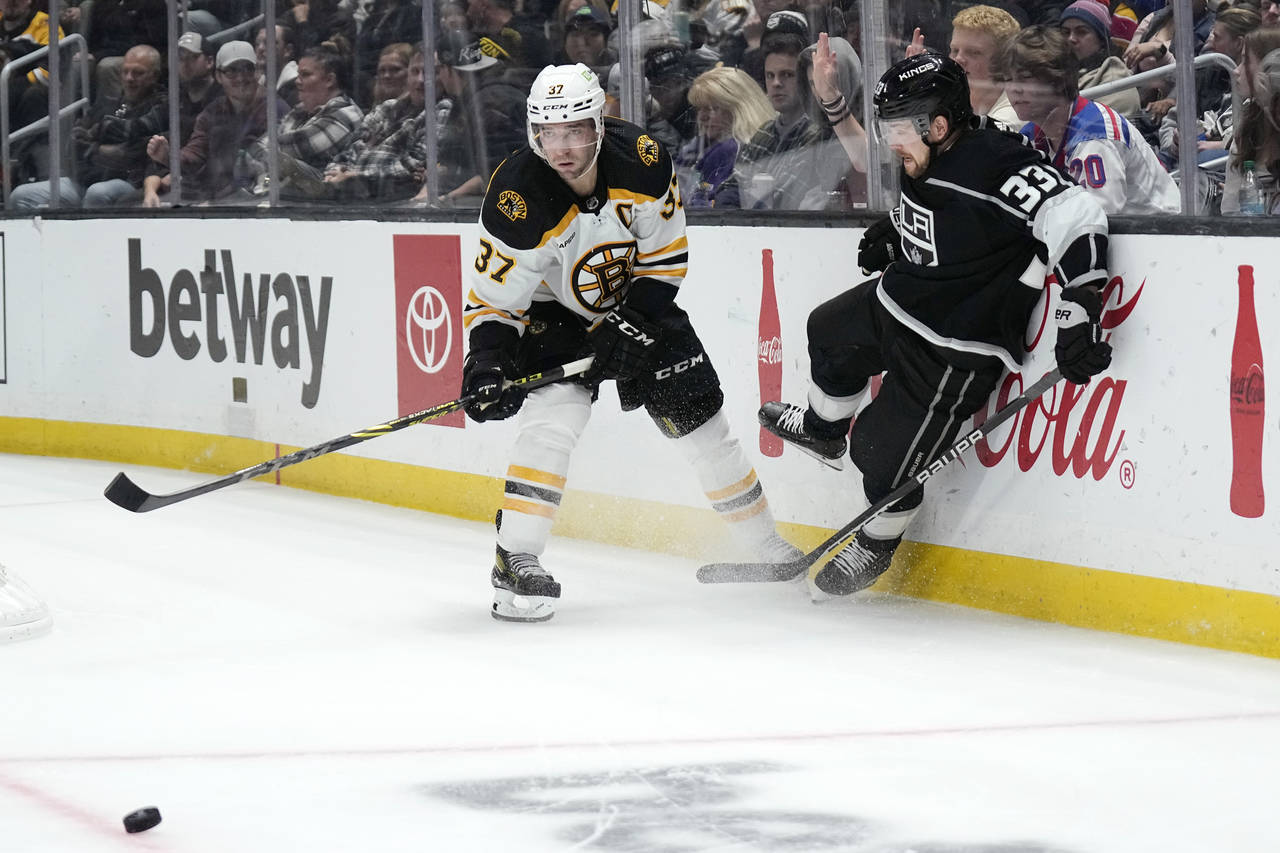 Boston Bruins center Patrice Bergeron, left, passes the puck as Los Angeles Kings right wing Viktor...