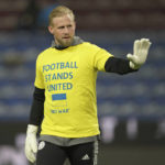 
              FILE -  Leicester's goalkeeper and Denmark international Kasper Schmeichel wears a T-shirt, saying 'Football Stands United - No War' with the flag of Ukraine on it, as he warms up prior to the English Premier League soccer match between Burnley and Leicester City at Turf Moor stadium in Burnley, England, on March 1, 2022. The players were wearing the shirts in protest against the Russian invasion of Ukraine. One year after the invasion of Ukraine began, Russia's reintegration into the world of sports threatens to create the biggest rift in the Olympic movement since the Cold War. (AP Photo/Jon Super)
            