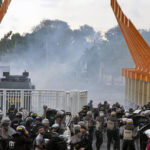 
              Riot police officers fire tear gas to disperse soccer supporters outside Jatidiri Stadium in Semarang, Central Java, Indonesia, Friday, Feb. 17, 2023. Indonesian police fired tear gas to disperse fans who were trying to force their way into a match that was held without spectators, months after the use of tear gas in another stadium in East Java caused one of the world's worst sporting disasters. (AP Photo/Adhik Kurniawan)
            