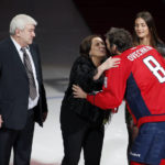 
              FILE - Mikhail Ovechkin, stands as his wife receives a kiss from their son, Washington Capitals left wing Alex Ovechkin, with his then-fiancé Nastya Shubskay, right, before he was presented a commemorative hockey stick by owner Ted Leonsis, Jan. 14, 2016, in Washington. Ovechkin says his father, Mikhail, has died. The Capitals captain delivered the news in Russian on his Instagram account. Ovechkin left the team yesterday to tend to a family health matter regarding a loved one. Coach Peter Laviolette said he expected Ovechkin to be gone for at least the rest of the week and away for the foreseeable future. (AP Photo/Alex Brandon, file)
            