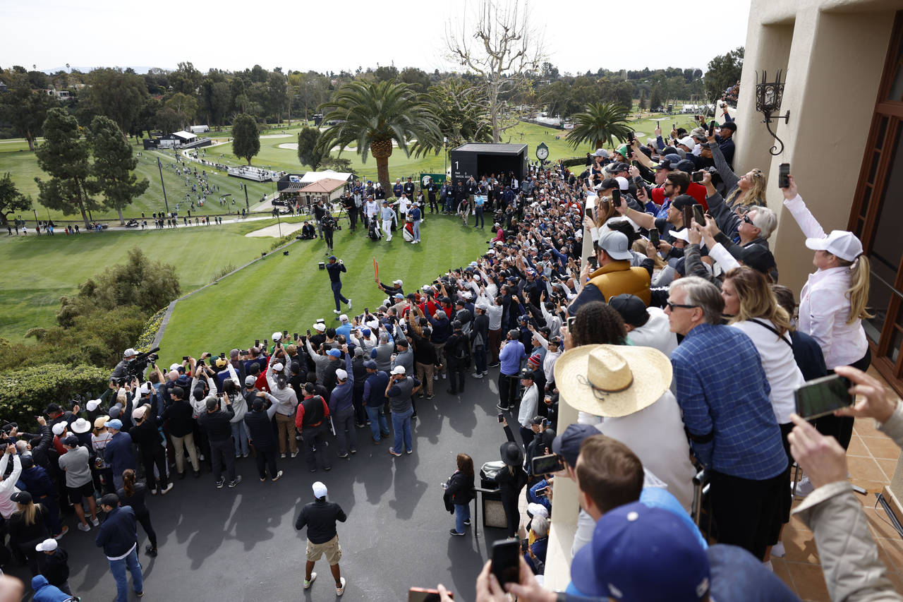 The gallery watches Tiger Woods, bottom left, as hits from the first tee during the first round of ...