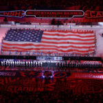 
              The Washington Capitals, left, and the Carolina Hurricanes stand as a large flag is unfurled during the national anthem before an NHL hockey Stadium Series game Saturday, Feb. 18, 2023, in Raleigh, N.C. (AP Photo/Chris Seward)
            