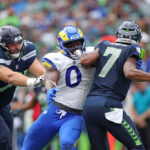 SEATTLE, WASHINGTON - SEPTEMBER 10:  Geno Smith #7 of the Seattle Seahawks is hit by Byron Young #0 of the Los Angeles Rams during the second half at Lumen Field on September 10, 2023 in Seattle, Washington. (Photo by Steph Chambers/Getty Images)