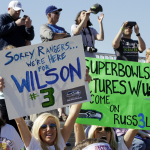 Seattle Seahawks fans hold up signs cheering on Seahawks quarterback Russell Wilson who worked out with the Texas Rangers during spring training baseball practice, Monday, March 3, 2014, in Surprise, Ariz. (AP Photo/Tony Gutierrez)