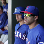 Seattle Seahawks quarterback Russell Wilson, right, stands by Texas Rangers' Brent Lillibridge in the dugout during a spring training exhibition baseball game against the Cleveland Indians, Monday, March 3, 2014, in Surprise, Ariz.