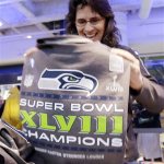 Julie Keim, of Mulkiteo, Wash., smiles as she unfolds a Seattle Seahawks' Super Bowl championship shirt to check on sizing at the team store, Monday, Feb. 3, 2014, in Seattle. The Seahawks defeated the Denver Broncos on Sunday in the Super Bowl XLVIII NFL football game, 43-8. (AP Photo/Elaine Thompson)