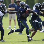 Seattle Seahawks running back Robert Turbin, second from left, carries the ball as wide receiver Percy Harvin, second from right, blocks Tharold Simon, right, and Terrance Parks pursues the tackle at left, during practice drills, Saturday, Aug. 2, 2014, at NFL football training camp in Renton, Wash. (AP Photo/Ted S. Warren)