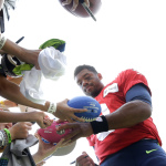 Seattle Seahawks quarterback Russell Wilson, right, signs autographs in a special "kids zone" fan section, Saturday, Aug. 2, 2014, after a session of NFL football training camp in Renton, Wash. (AP Photo/Ted S. Warren)
