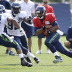 Seattle Seahawks quarterback Russell Wilson, right, keeps the ball as he tries to avoid the defense of linebacker Marcus Dowtin (38) and defensive end Benson Mayowa (95), Saturday, Aug. 2, 2014, during NFL football training camp in Renton, Wash. (AP Photo/Ted S. Warren)